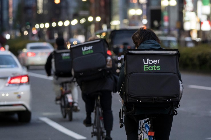 Several Uber Eats delivery bicyclists in Tokyo are seen from behind delivering food with packs on their back that say "Uber Eats."
