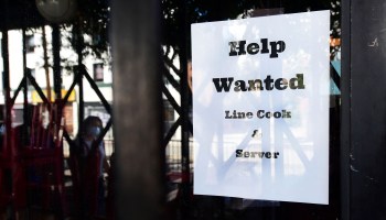 Pedestrians pass a "Help Wanted" sign posted at restaurant looking for line cooks and servers.