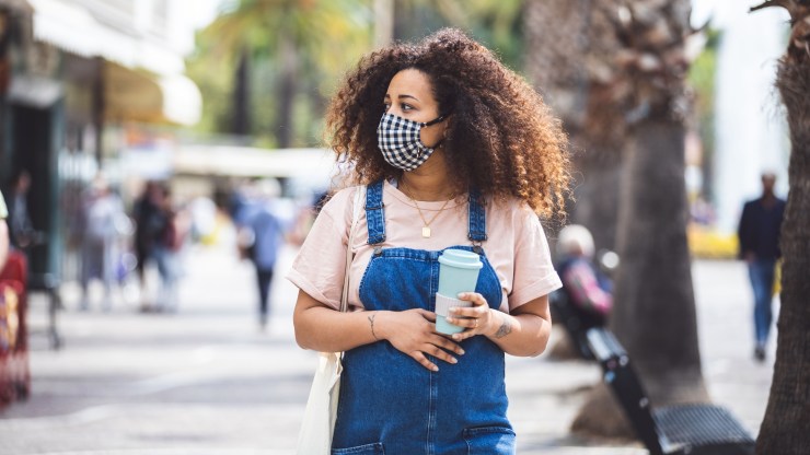 Pregnant woman walking in the city in a sunny day protecting herself with a cloth face mask in Italy during Covid-19 coronavirus pandemic