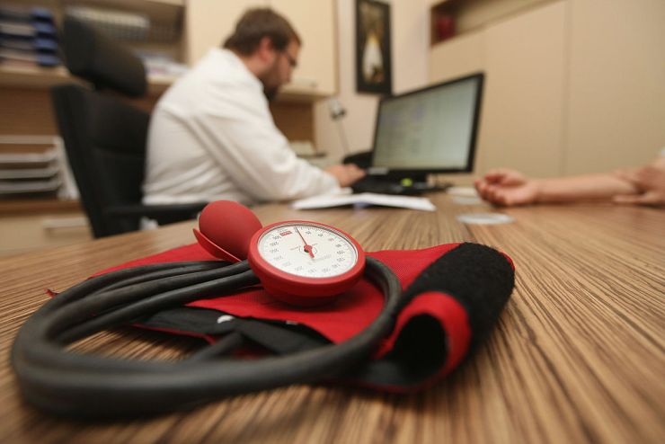 A blood pressure monitor lies on doctor's desk as he speaks to his patient.
