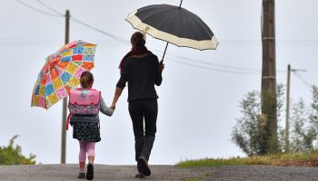 A mother and daughter walk hand-in-hand while holding umbrellas