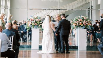 A bride and groom stand before an officiant, with guests sitting behind them.