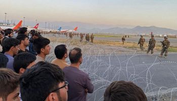 Afghans line up behind barbed wire at Kabul airport with soldiers on the other side of the fence