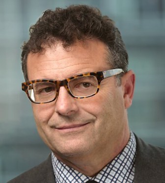 George Selgin poses for his headshot wearing glasses and a plaid collared shirt in front of a blurry neutral background.