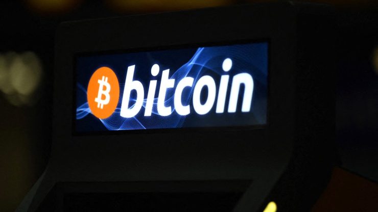 A bitcoin ATM with a blue and white glowing sign shows the word "bitcoin" alongside the orange and white "B" icon. It is an ATM locate within a Salvadoran shopping center.