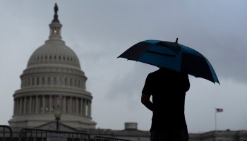 A man holds an umbrella as it begins to rain near the U.S. Capitol.