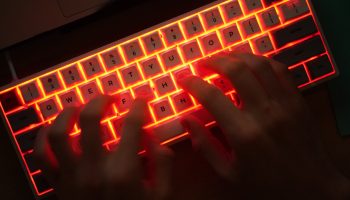 Hands rest on an orange-lit computer keyboard as they type.