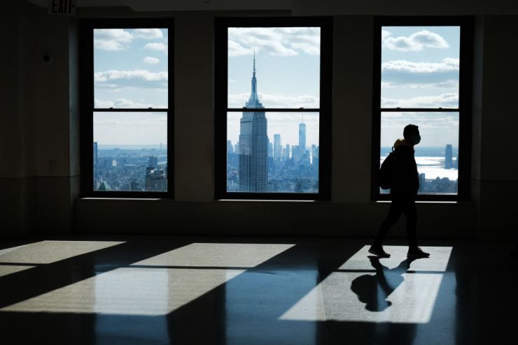 A figure in silhouette walks through an empty office building with a view of Manhattan outside the the tall windows.
