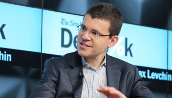 Max Levchin, CEO of Affirm, wears a navy blazer and glasses. He sits onstage in front of a screen, lifts his hand, and speaks to a fellow panelist.