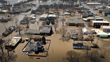 Over a dozen buildings can be seen surrounded by brown floodwater.