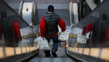 A man carries his purchases, including a package of toilet paper, down an escalator through the Sarbanes Transit Center on April 16, 2020 in Silver Spring, Maryland.