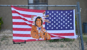 An American flag with an image of Native American on it is attached to a fence outside a home in the East To'Hajiilee housing community in To’Hajiilee Indian Reservation, New Mexico.