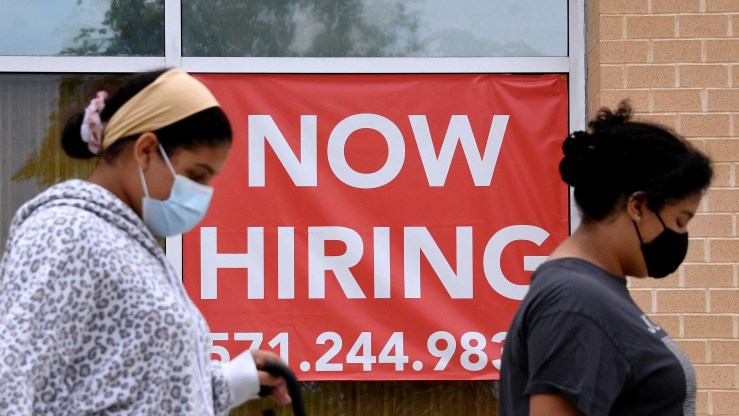 Women walk past by a "Now Hiring" sign outside a store on August 16, 2021 in Arlington, Virginia.
