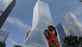 A construction worker stands in front of a tall skyscraper in China.
