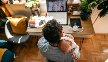 A father holds his baby while working at his computer.