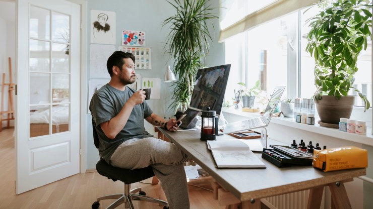 A digital worker looks at his computer screen during a coffee break in his home office.
