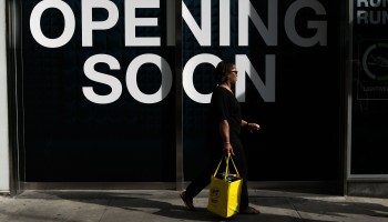 A woman carrying a shopping bag walks past a soon-to-open storefront in Manhattan.
