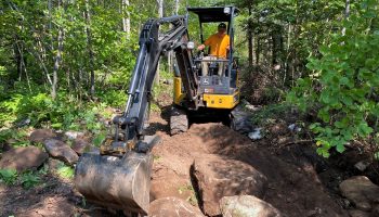 Adam Harju uses a three-ton excavator to move huge rocks into place on a new mountain bike trail he’s building near Split Rock Lighthouse State Park on Aug. 9.