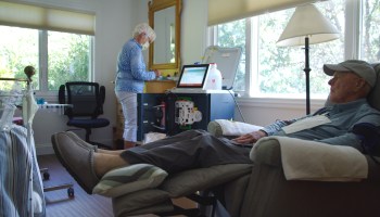Liz Henry uses the Tablo dialysis machine in the background while Dick Henry lays on a reclining chair in the foreground.