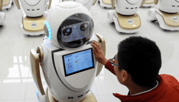 An employee at a factory in China checks a robot used in customer service. the robot has a cartoon face with a screen on its chest.