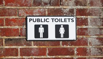 A sign reading "public toilets" with icons for men's and women's restrooms on a brick wall.