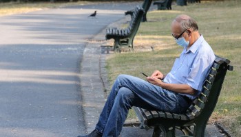A man with a face mask sits on a bench at an urban park. More benches, public restrooms and services for unhoused people could be part of a care-driven approach to designing cities.