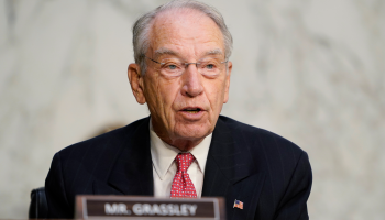 Sen. Chuck Grassley (R-IA) speaks at a podium wearing a navy suit and red tie.