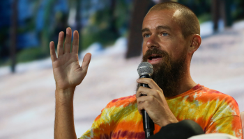 Twitter CEO and founder Jack Dorsey, wearing an orange, red and yellow tie-dye shirt speaks into a microphone.