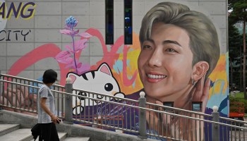A woman walks past a mural showing an image of rapper RM from the K-pop boy band BTS