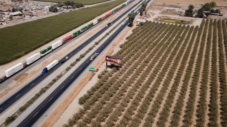 In this aerial image, vehicles drive on US Highway 99 past farmland and a freight train through Tulare County in the Central Valley near Pixley, California.