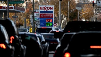 An Exxon sign shows gas prices at $3.45 and $3.89 a gallon as cars pass by.