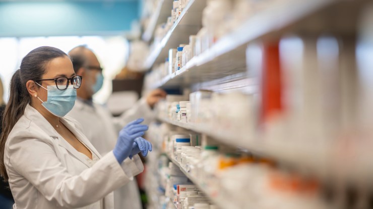 A pharmacist arranges medicines on a shelf.