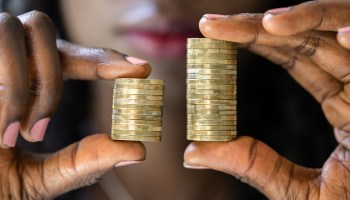 A Black woman holds a stack of coins in each hand, one taller than the other.