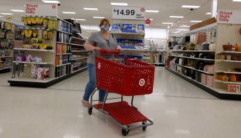 A woman wearing a face mask, gray T-shirt and jeans pushes a red shopping cart in front of aisles at a Target in September in Miami.