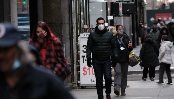 People in Manhattan walk down a street wearing coats and masks.