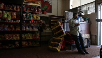 Grocery store owner Mahmod Alrihimi waits for customers while leaning against his checkout counter.