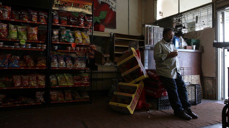 Grocery store owner Mahmod Alrihimi waits for customers while leaning against his checkout counter.