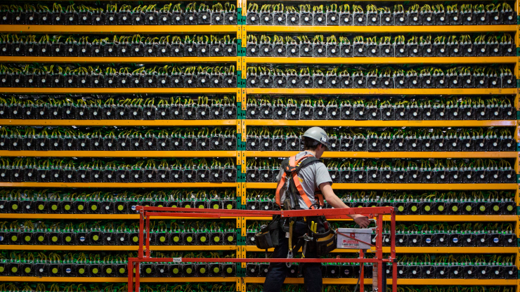 A technician stands on an elevated platform in a hard hat looking at dozens of computers and their fans in rows mining bitcoin Quebec in 2018.