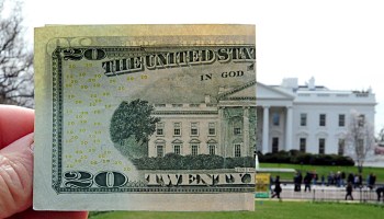 A $20 bill with the White House in the background.