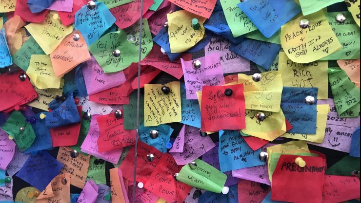 Pieces of brightly colored confetti with handwritten wishes on them, pinned to a billboard in Times Square in December 2021.