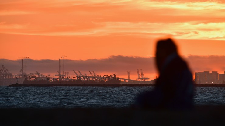 The Port of Long Beach is seen in the distance as a woman views the sunset from Sunset Beach in Huntington Beach, California on July 21, 2018.