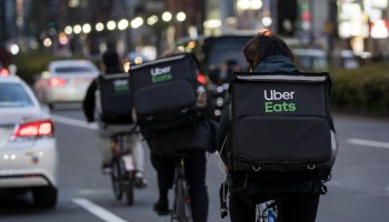 Three people on bicycles toting food courier bags labeled "Uber Eats" ride down a street.