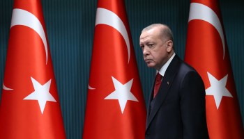 Turkish President Recep Tayyip Erdoğan stands in front of three Turkish flags.