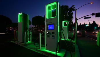 At sunset, an electric vehicle charging station is seen with glowing green lights.