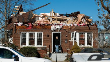 A homeowner stands at the doorstep of a single-story brick home with the roof torn off in Bowling Green, Kentucky..