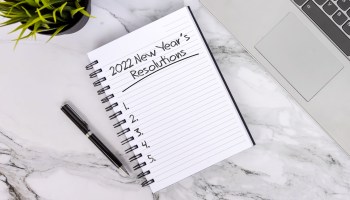 A notebook on a table reads "2022 New Year's Resolutions" with Nos. 1 through 5 left blank.ns.