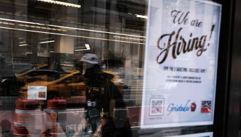 A "We are hiring!" sign is displayed in a New York store window.