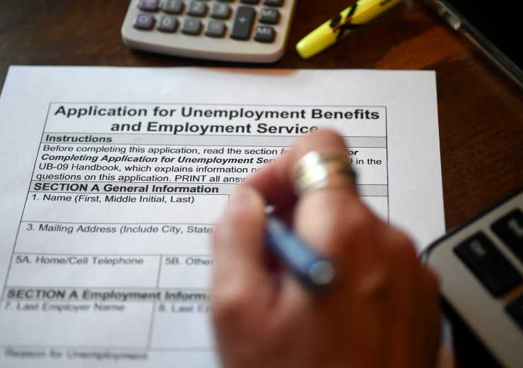 A close-up image of a hand with pen filling out an application for unemployment benefits.