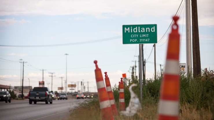 A city limit sign for Midland, Texas, in 2020, with cars driving in the background.
