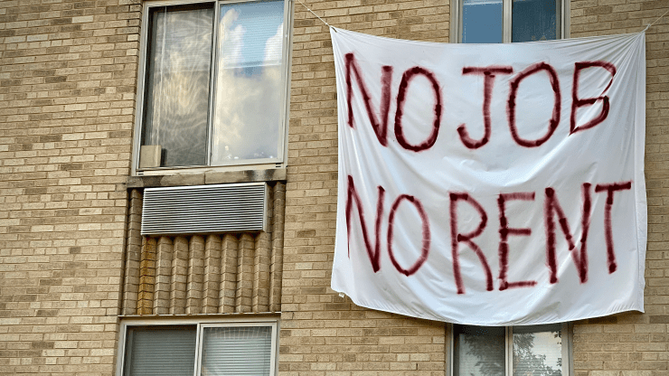 A white banner with the phrase, "No Job, No Rent" hangs on the exterior of a beige apartment building in Washington, D.C.